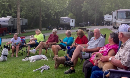 Group of people sitting outdoors in chairs with their dogs